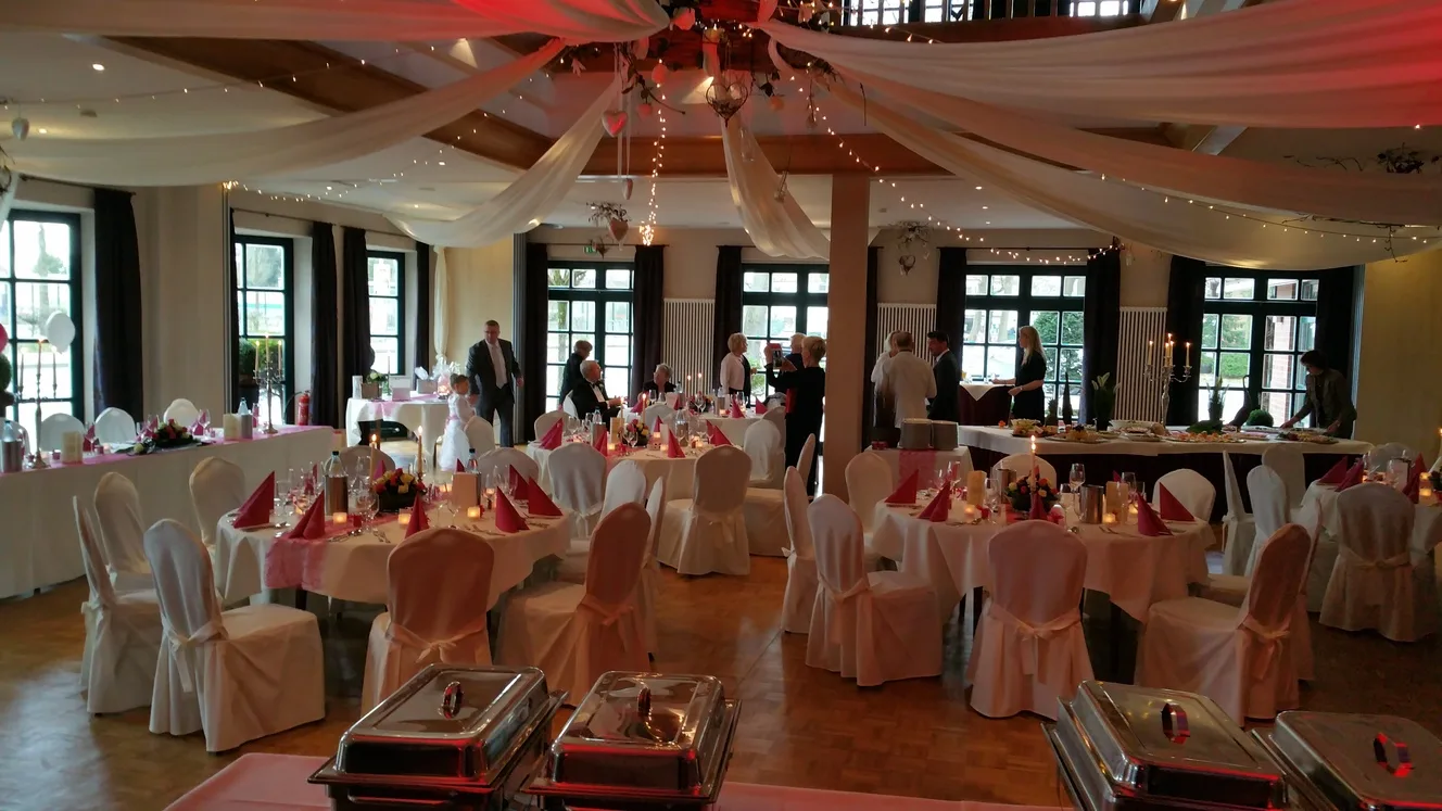 Festlich eingedeckter Saal mit weißen Stuhlhussen und Buffet